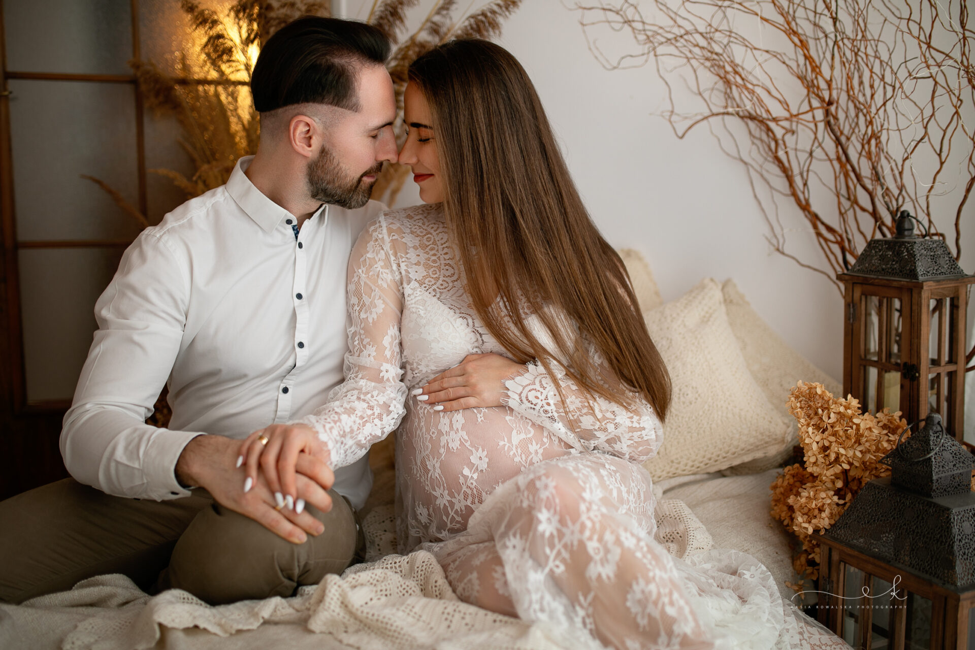 portret zakochanej pary oczekującej na narodziny dziecka, dotykają się nosami i się się uśmiechają - studyjna sesja ciążowa w stylu boho Kraków