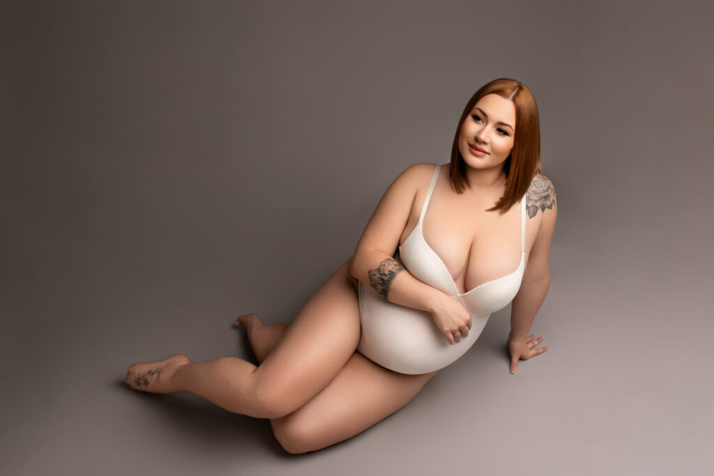 minimalistyczna sesja ciążowa w studio, kobieta w ciąży w białym body siedzi na podłodze