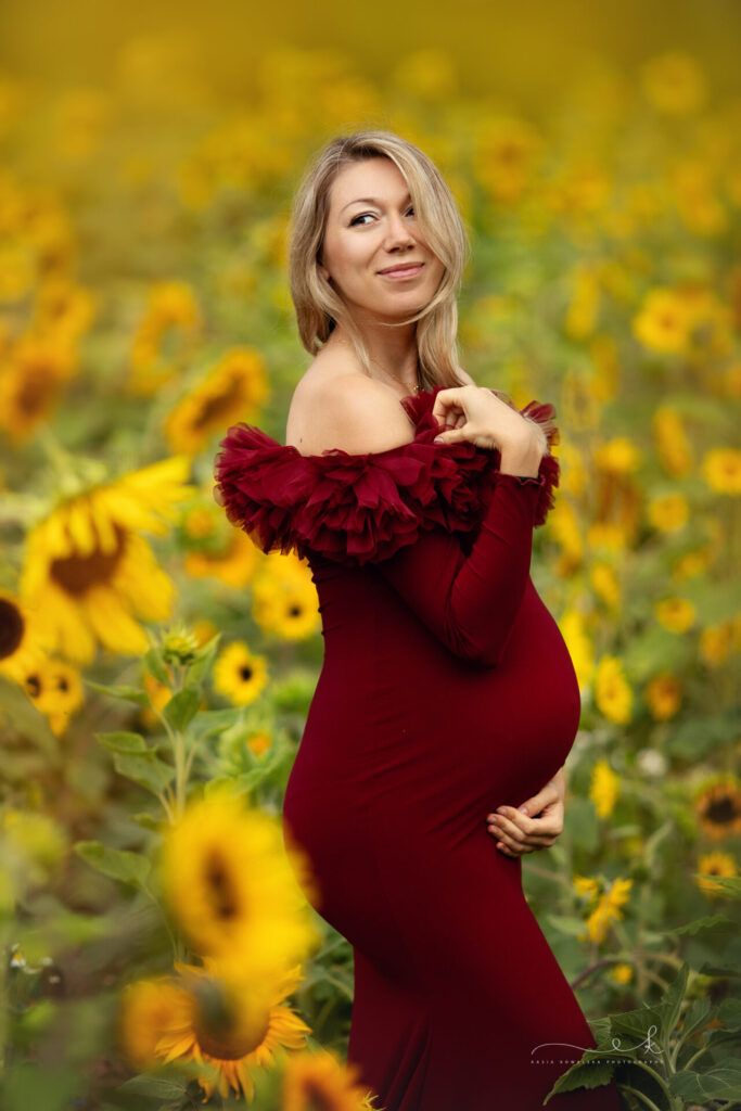 Kobieta w ciąży w bordowej sukience na polu słonecznikow